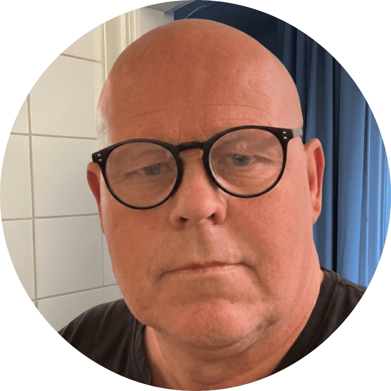 Porträtt av skallig man med glasögon och neutralt ansiktsuttryck.